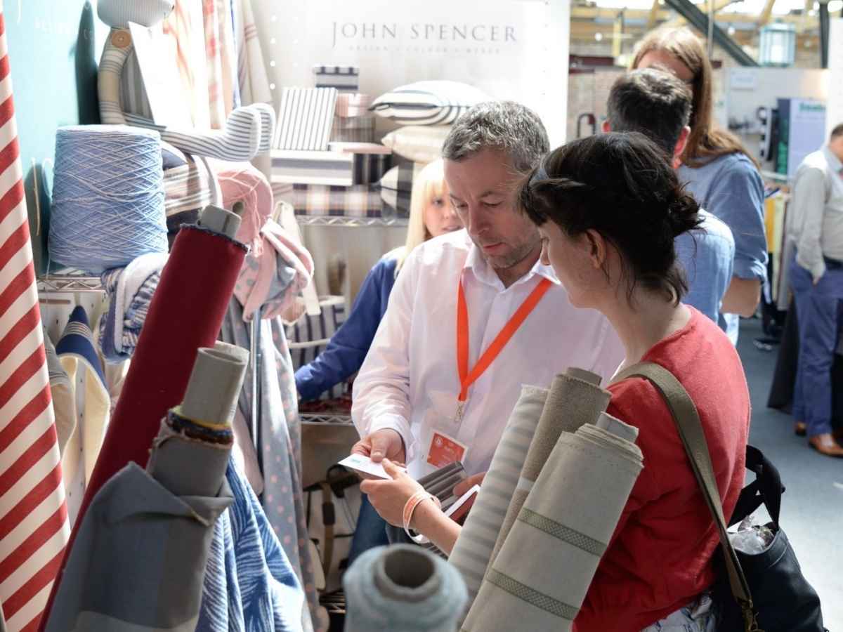 A visitor looking at fabric with an exhibitor on the John Spencer Textiles stand